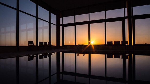 A room with large windows reflecting the sunset, a pool, and several chairs. - Hotel Dolphin (Senec)