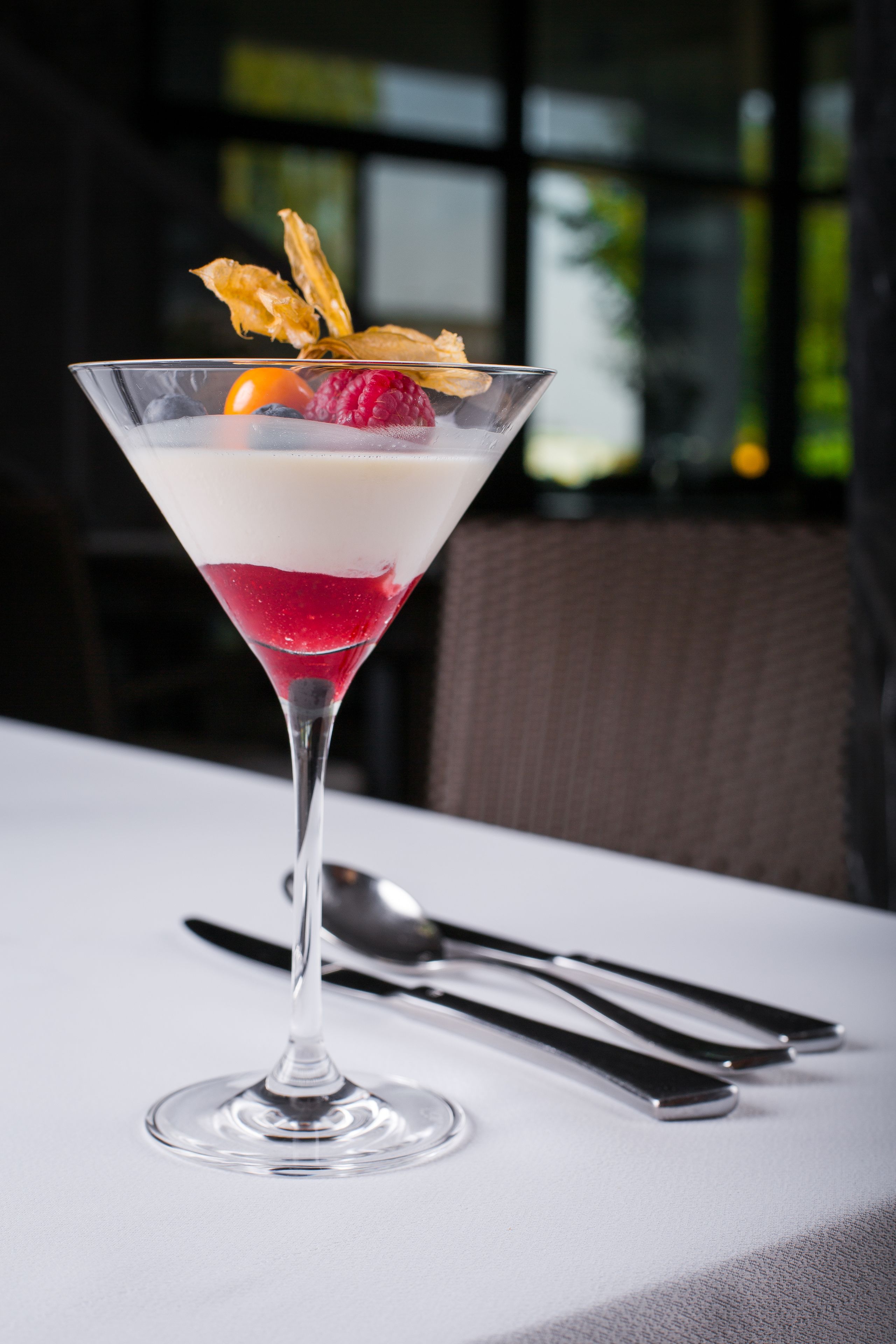 A dessert in a martini glass with a white and red layer, garnished with a raspberry and a wafer.
