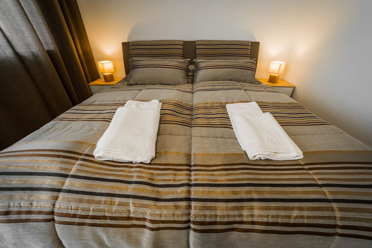 Una cama bien hecha con ropa de cama a rayas y dos toallas dobladas al pie.
