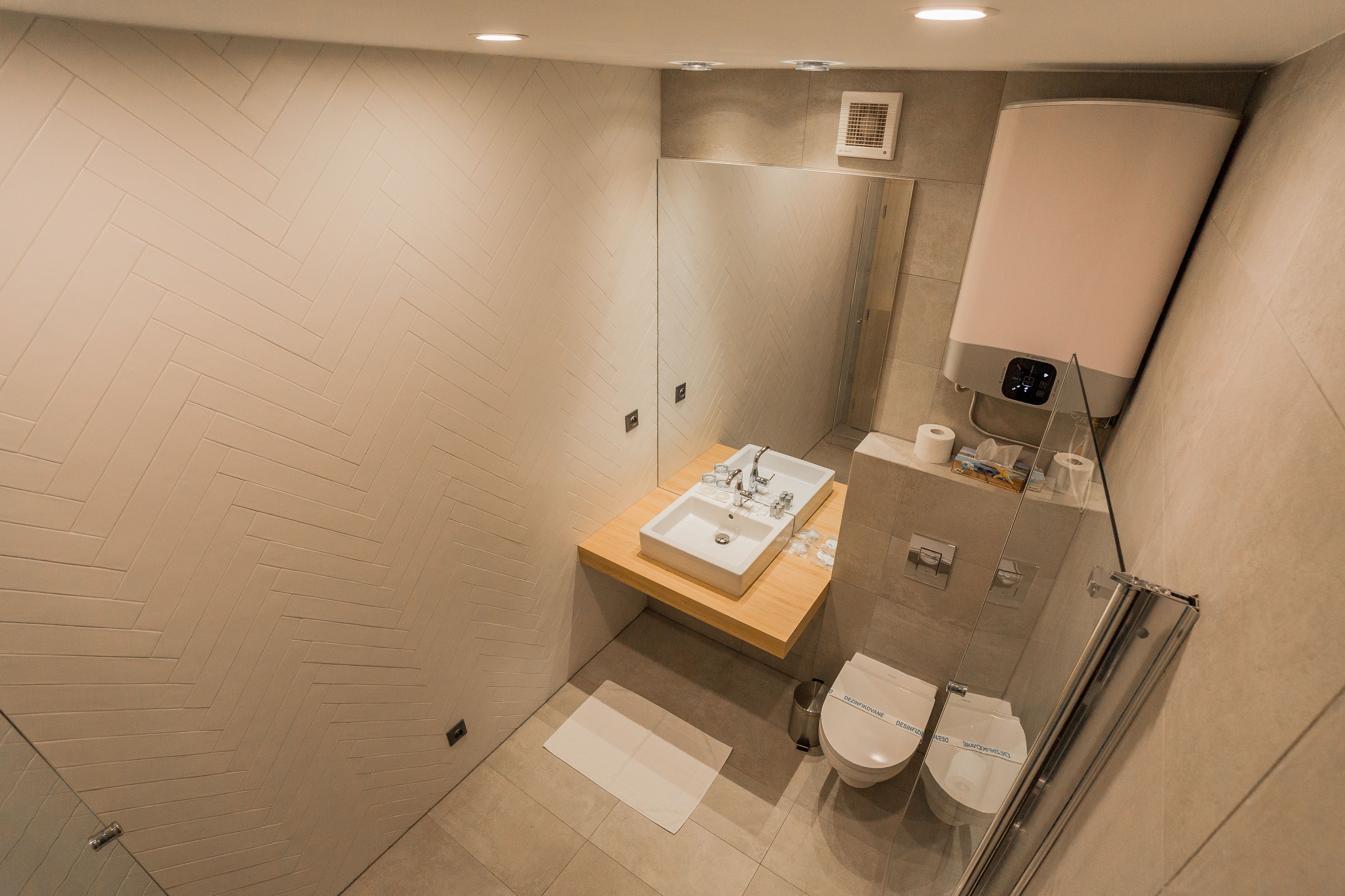 A modern bathroom with a herringbone floor pattern, a wooden vanity with a sink, a glass shower enclosure, and two toilets.