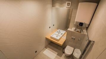A modern bathroom with a herringbone floor pattern, a wooden vanity with a sink, a glass shower enclosure, and two toilets.