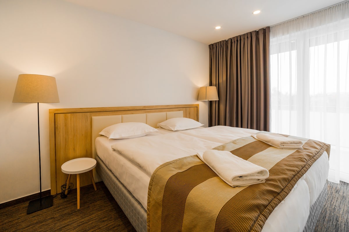 Una cama bien hecha con cabecera de madera, dos lámparas de noche y una mesita redonda al lado.