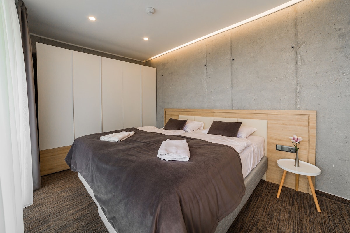 Habitación de hotel moderna con una cama grande, una mesita de noche con un florero y un panel de control en la pared.