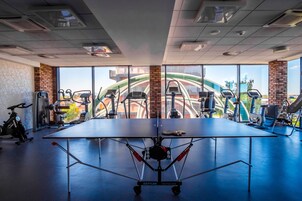 Un gimnasio con mesa de ping pong, equipamiento de ejercicio y amplias ventanas con vistas a la ciudad.