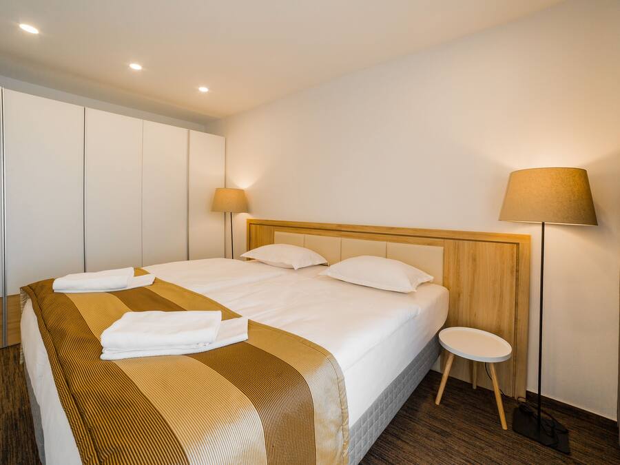 A hotel room with a large bed, two bedside lamps, a wooden headboard, and a small round table.