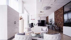 A modern living room with white furniture, a glass coffee table, and a brick accent wall. - Hotel Dolphin (Senec)