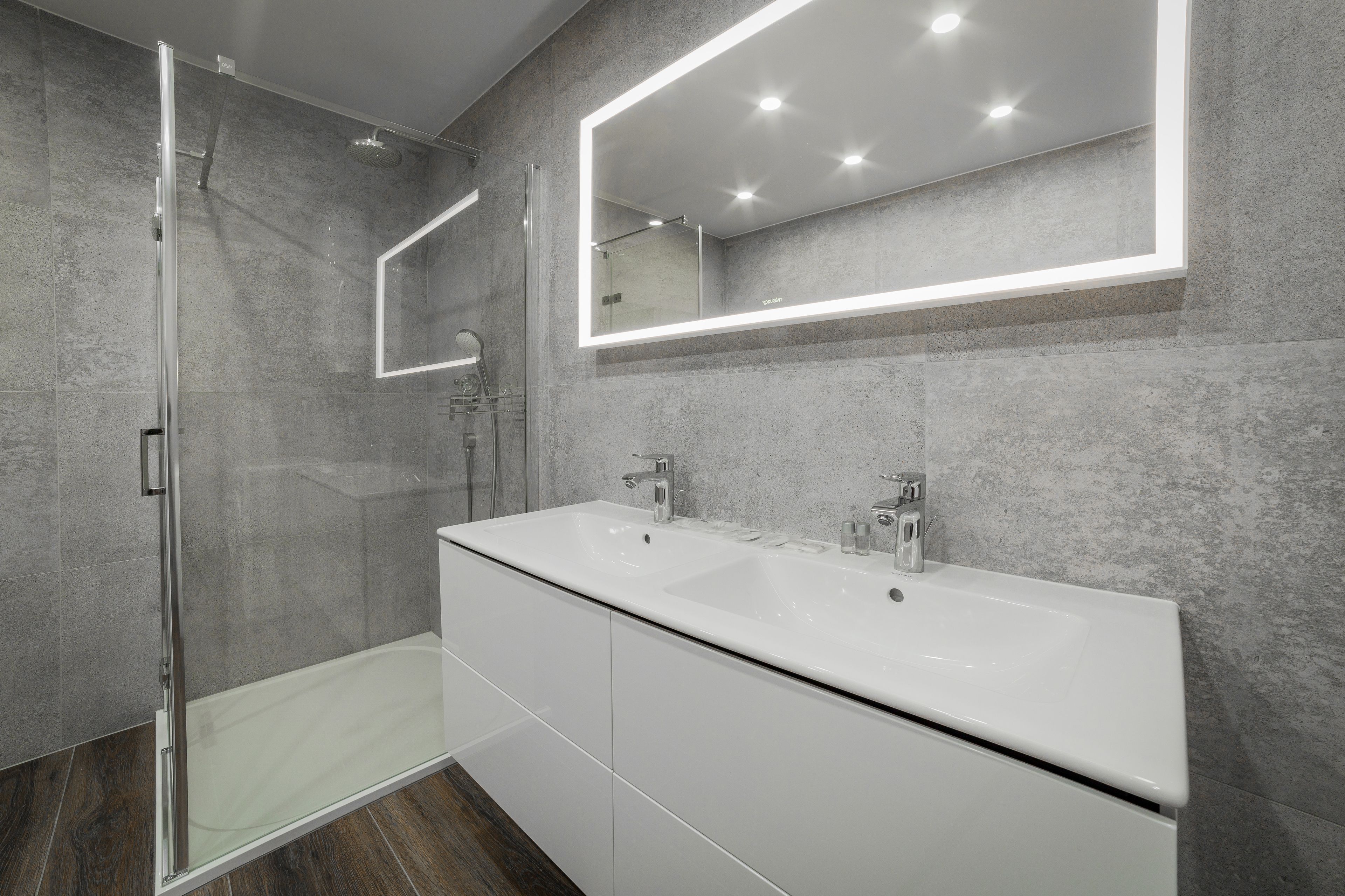 A modern bathroom with a glass-enclosed shower, a large mirror, and a white vanity with two sinks.