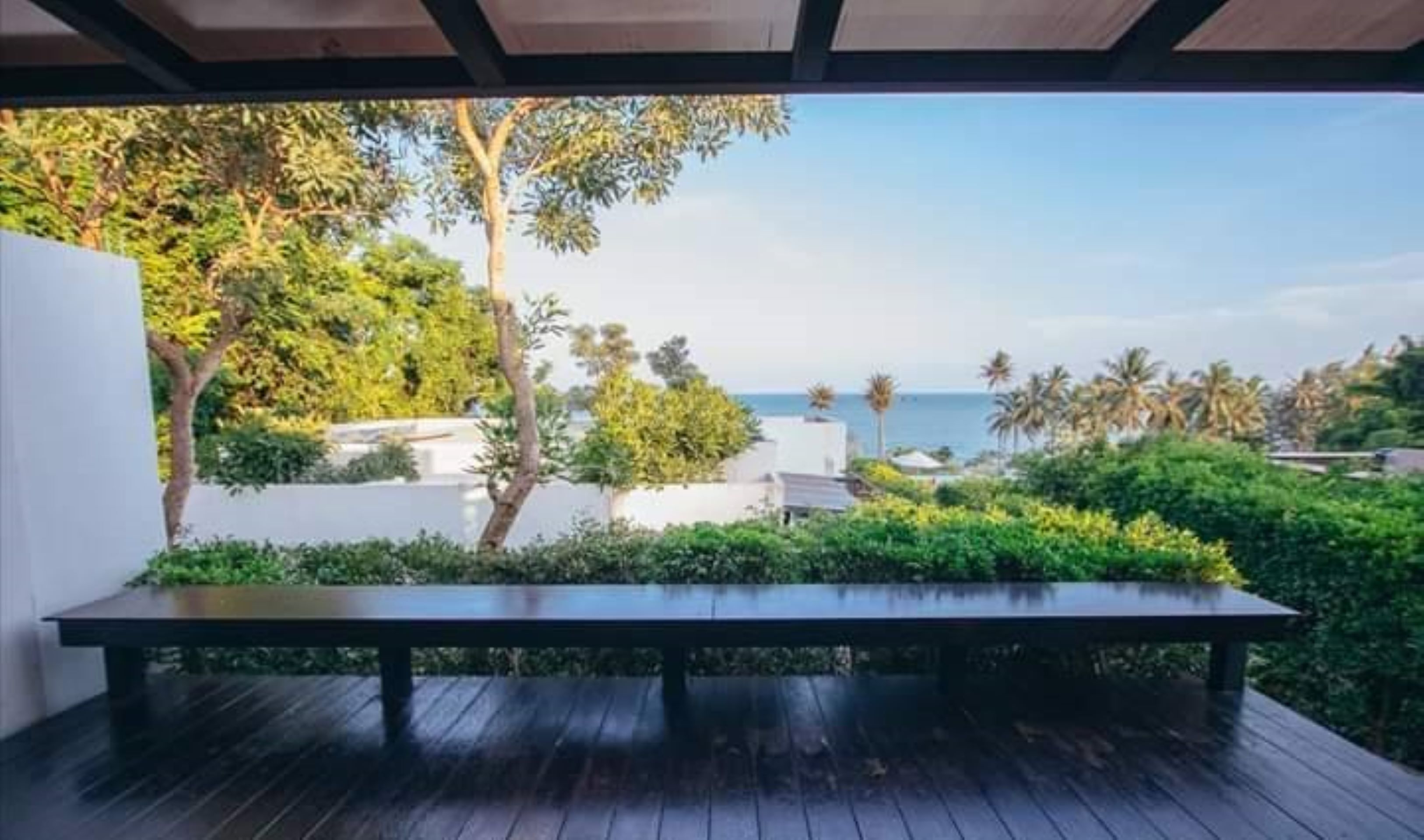 An outdoor seating area with a view of the sea and palm trees.