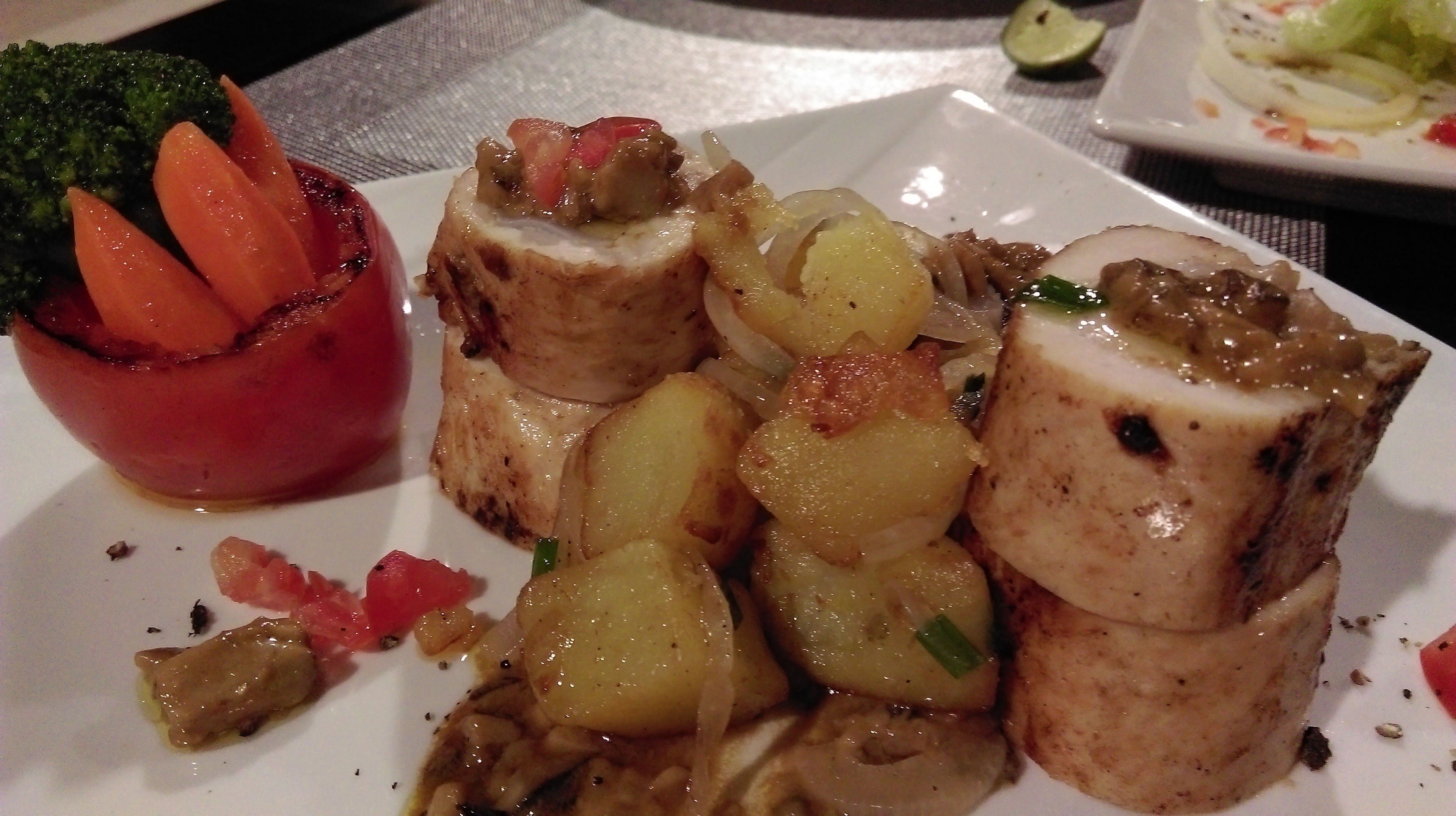 Un plato de comida con pechuga de pollo rellena, papas asadas y un guiso de verduras rojas.