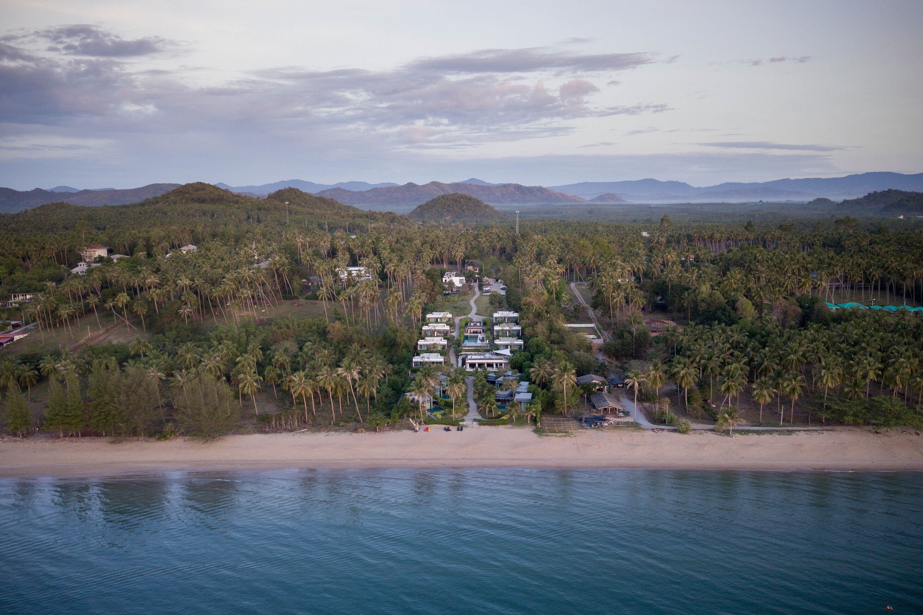 Vista aérea de un complejo turístico costero con varias villas, una playa y palmeras.