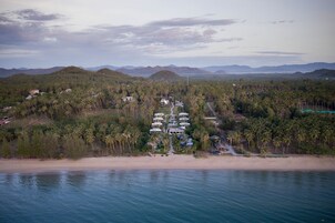 Vista aérea de un complejo turístico costero con varias villas, una playa y palmeras.