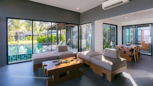 Un salón moderno con vista a una piscina, ventanas amplias y una mesa de centro de madera.
