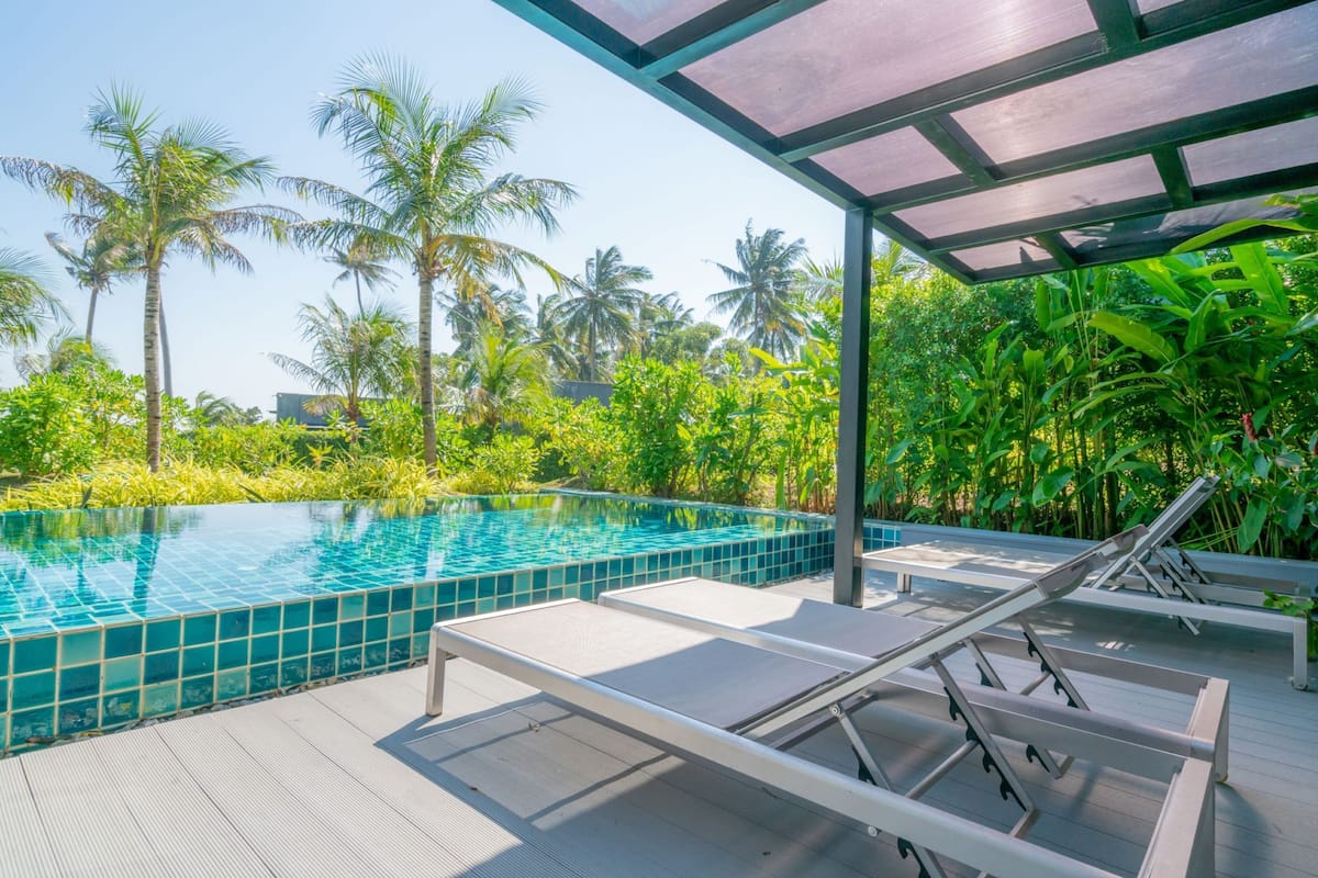 A swimming pool with lounge chairs and a covered area, surrounded by palm trees and greenery.