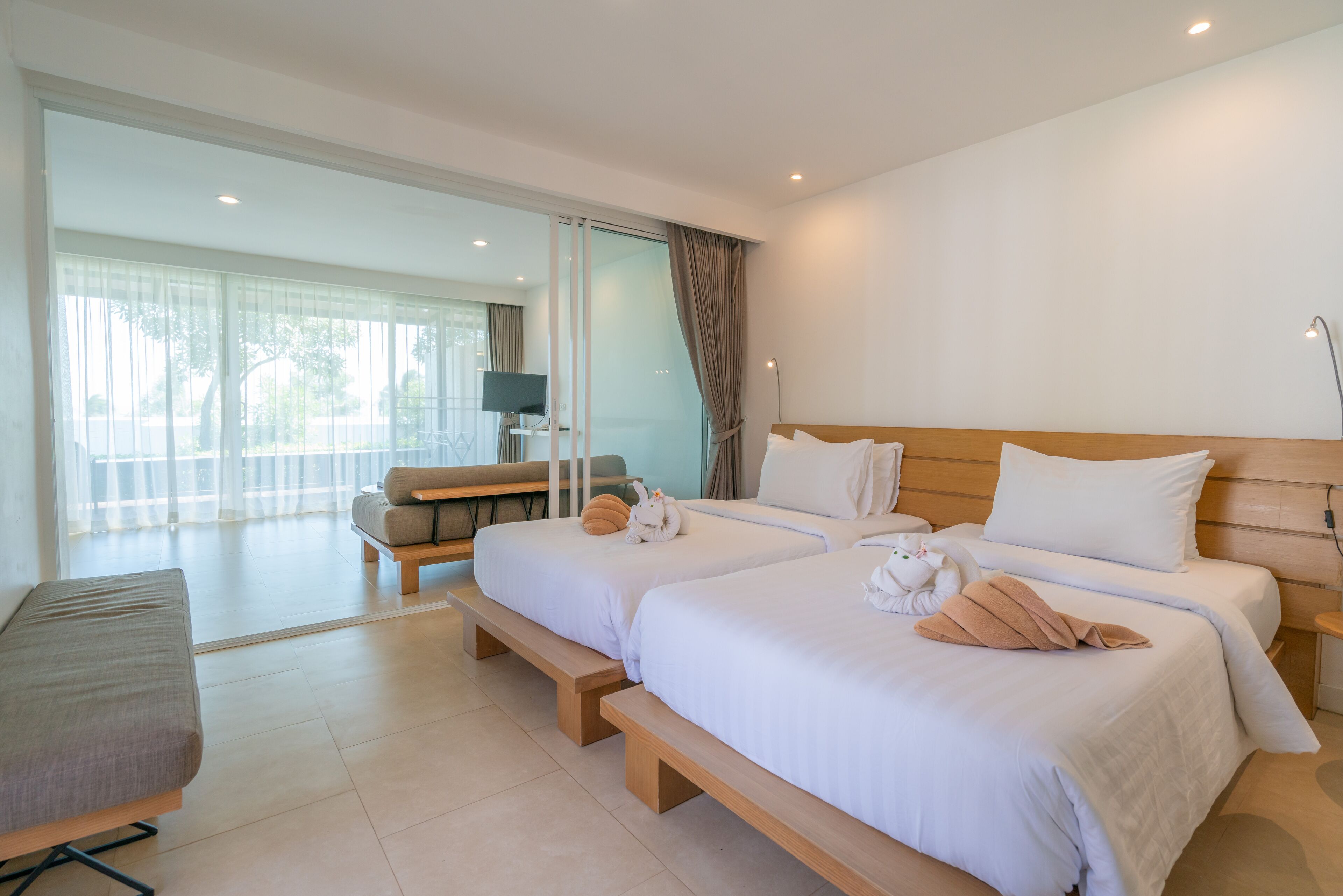Una habitación de hotel moderna con dos camas, un banco, un sofá y un televisor.