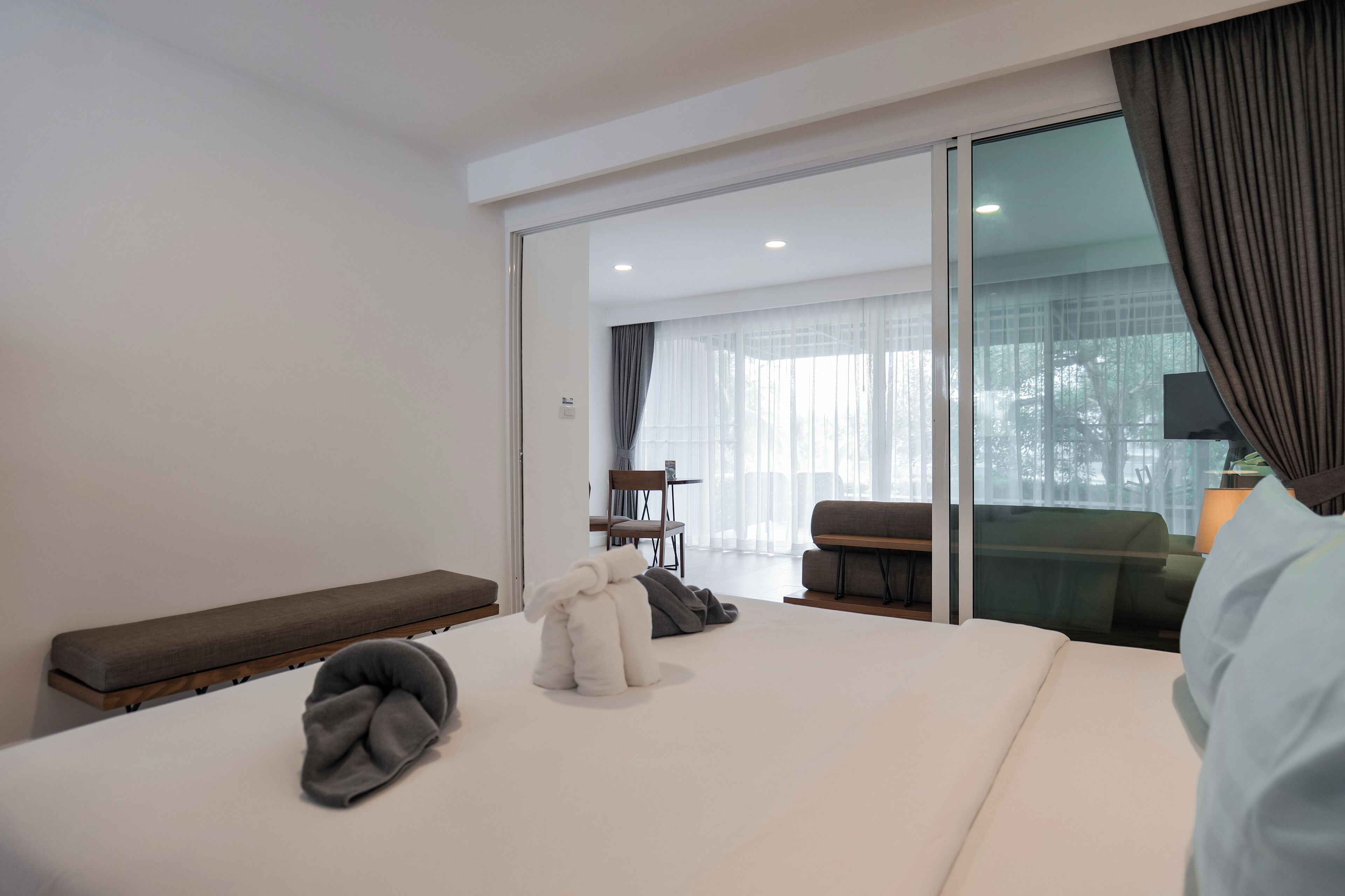Una habitación de hotel moderna con una cama grande, un banco, una zona de estar con una mesa y vistas a través de un ventanal.