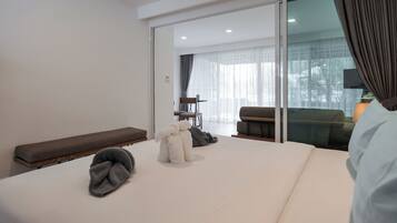 Una habitación de hotel moderna con una cama grande, un banco, una zona de estar con una mesa y vistas a través de un ventanal.