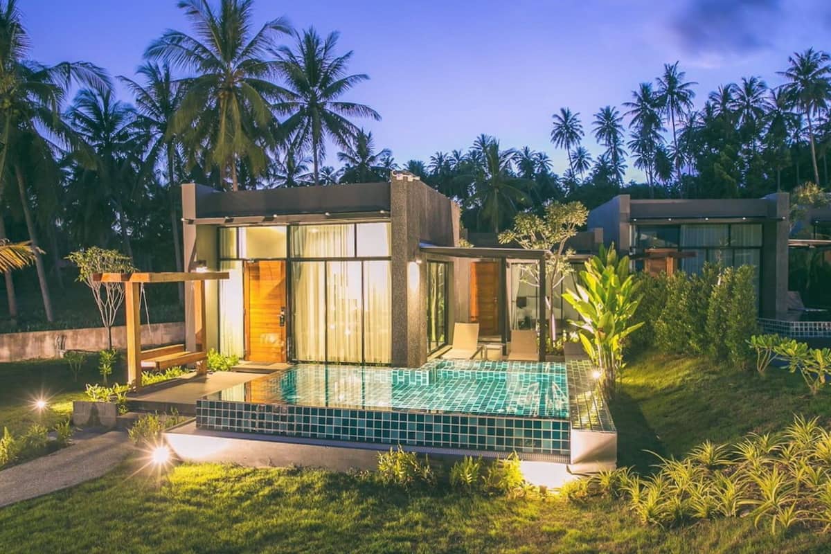 A modern house with a swimming pool, surrounded by lush greenery and palm trees.