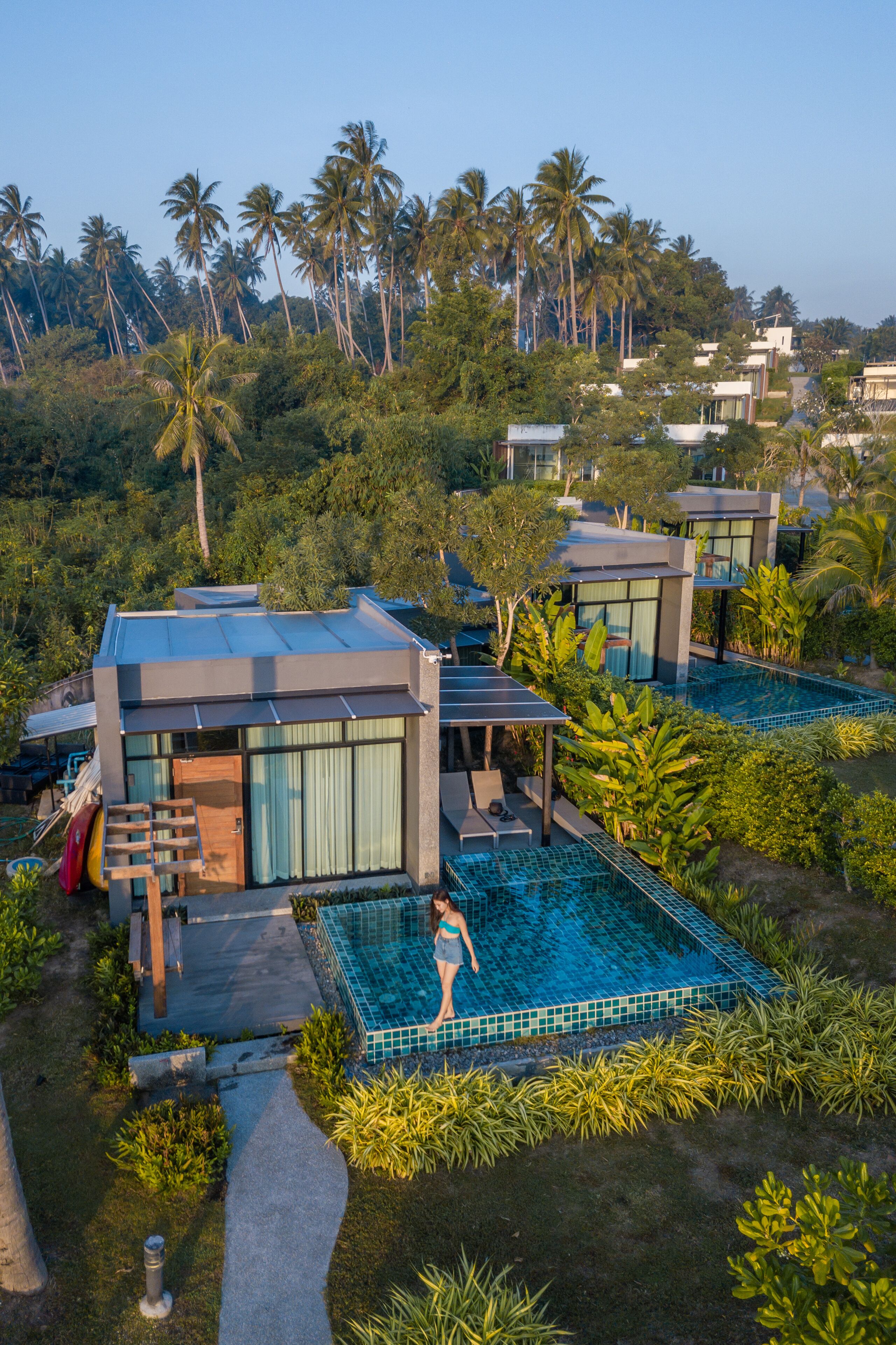 Un complexe hôtelier moderne doté d’une piscine, d’une terrasse couverte et d’un environnement tropical luxuriant.