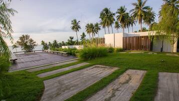 A modern outdoor area with a wooden deck, grassy patches, palm trees, and a white building with vertical slats.