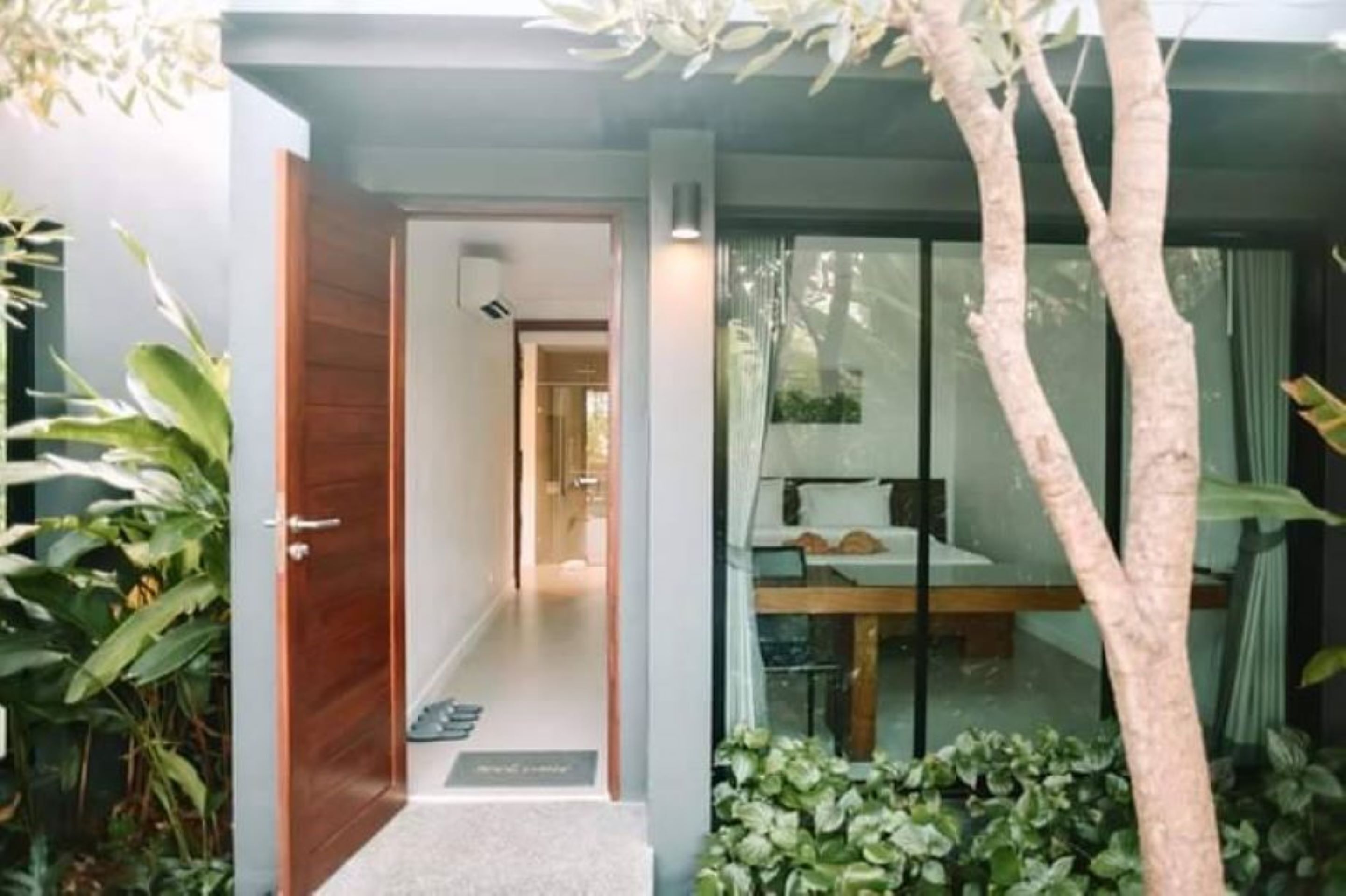 Un intérieur moderne avec une porte en bois donnant sur un couloir, un coin repas avec une table et des chaises, et une grande fenêtre avec des rideaux.