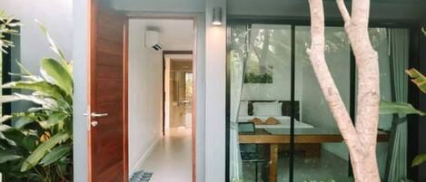 Un intérieur moderne avec une porte en bois donnant sur un couloir, un coin repas avec une table et des chaises, et une grande fenêtre avec des rideaux.