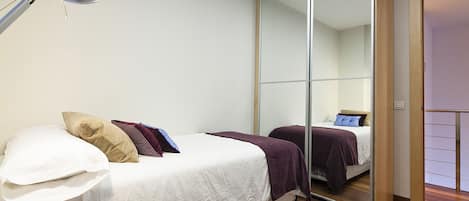 A bedroom with a bed, a bedside lamp, a mirror, and a wooden floor.