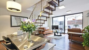 A modern living room with a staircase, a dining area with a table and chairs, a sofa, and a large window offering a view of the outside. - MSB Pool with Terrace (Barcelona)