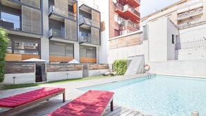 A modern apartment building with a swimming pool, wooden deck, and red lounge chairs. - MSB Pool with Terrace (Barcelona)