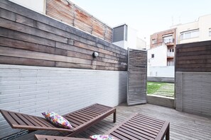 Una terraza de madera con dos bancos de madera y un portón metálico entreabierto.
