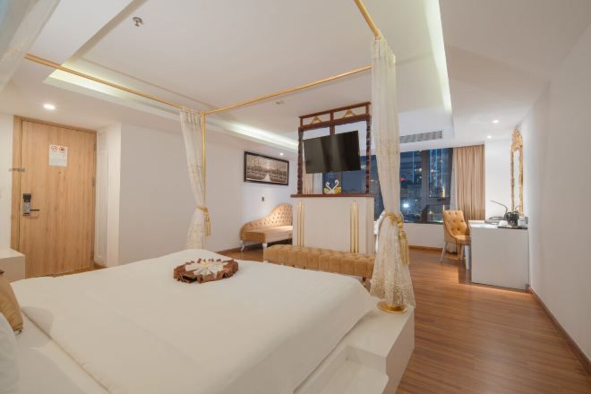 A modern hotel room with a large bed, a desk, and a view of the city at night.