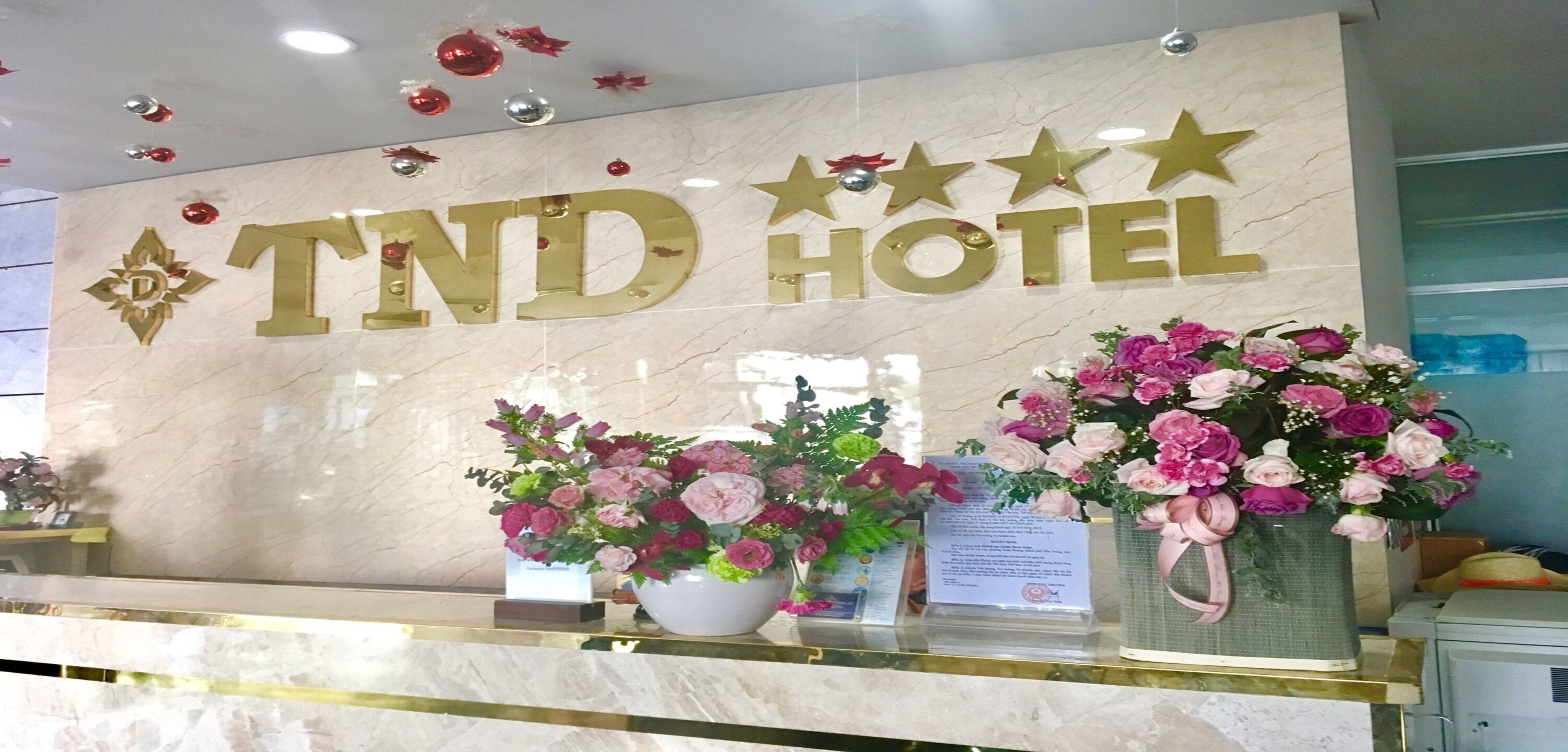 Een receptiebalie bij Hotel TND met een marmeren aanrechtblad, grote bloemstukken en een bord met sterren en de naam van het hotel.