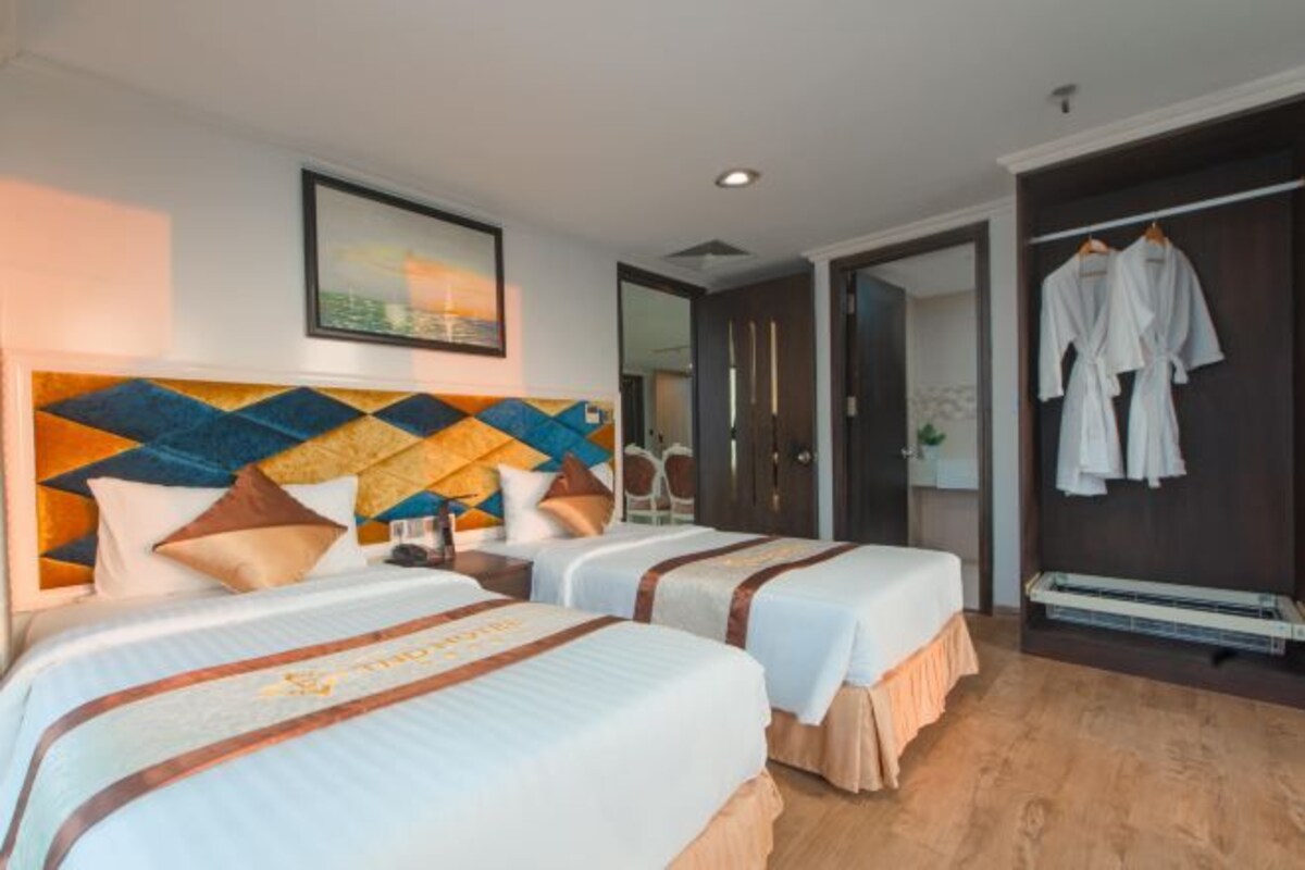 A hotel room with two beds, a modern headboard, a painting, and a wardrobe with robes.