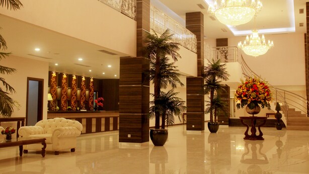 Een ruime lobby met een hoge plafond, kroonluchters, een receptiebalie en potplanten.