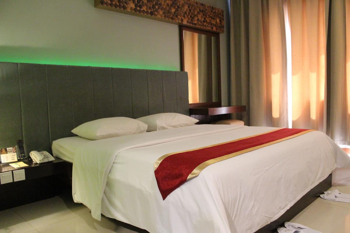 Une chambre d’hôtel avec un grand lit, une table de chevet avec un téléphone et une petite table de nuit avec une lampe.