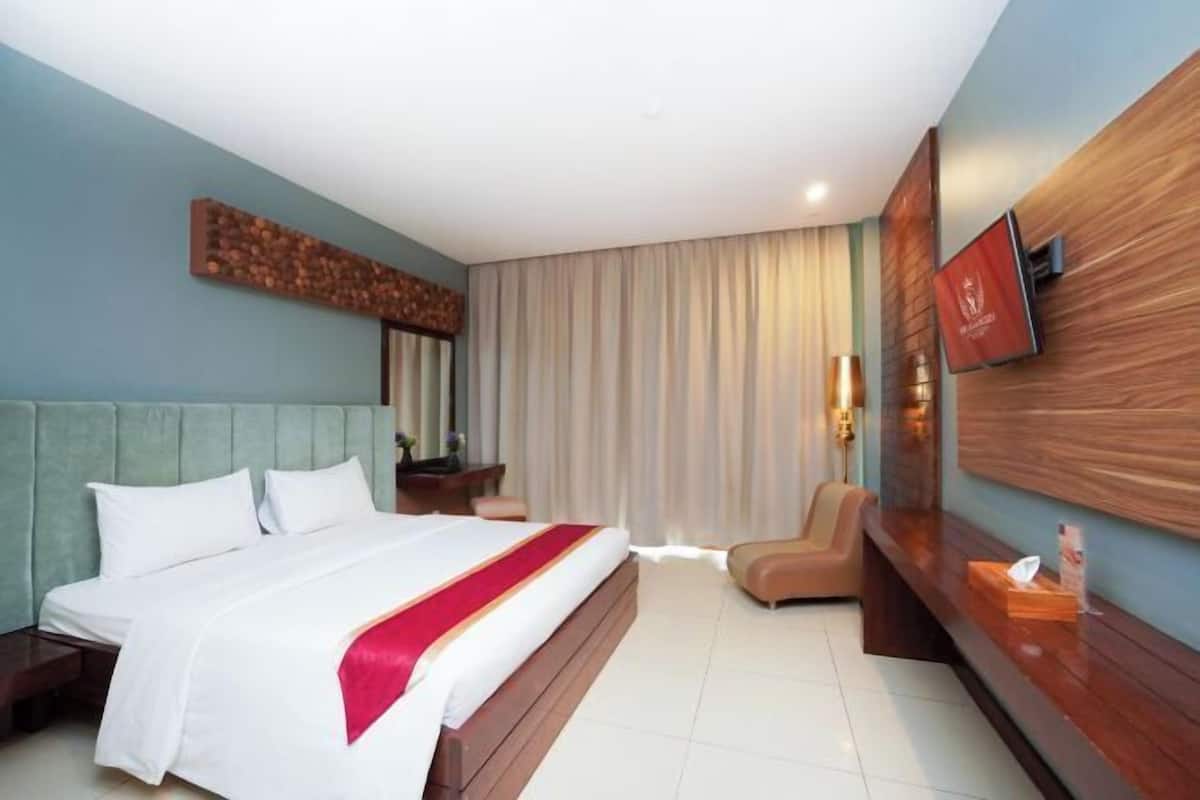 Une chambre d’hôtel avec un lit, une tête de lit en bois, un téléviseur fixé au mur, un bureau et une chaise.