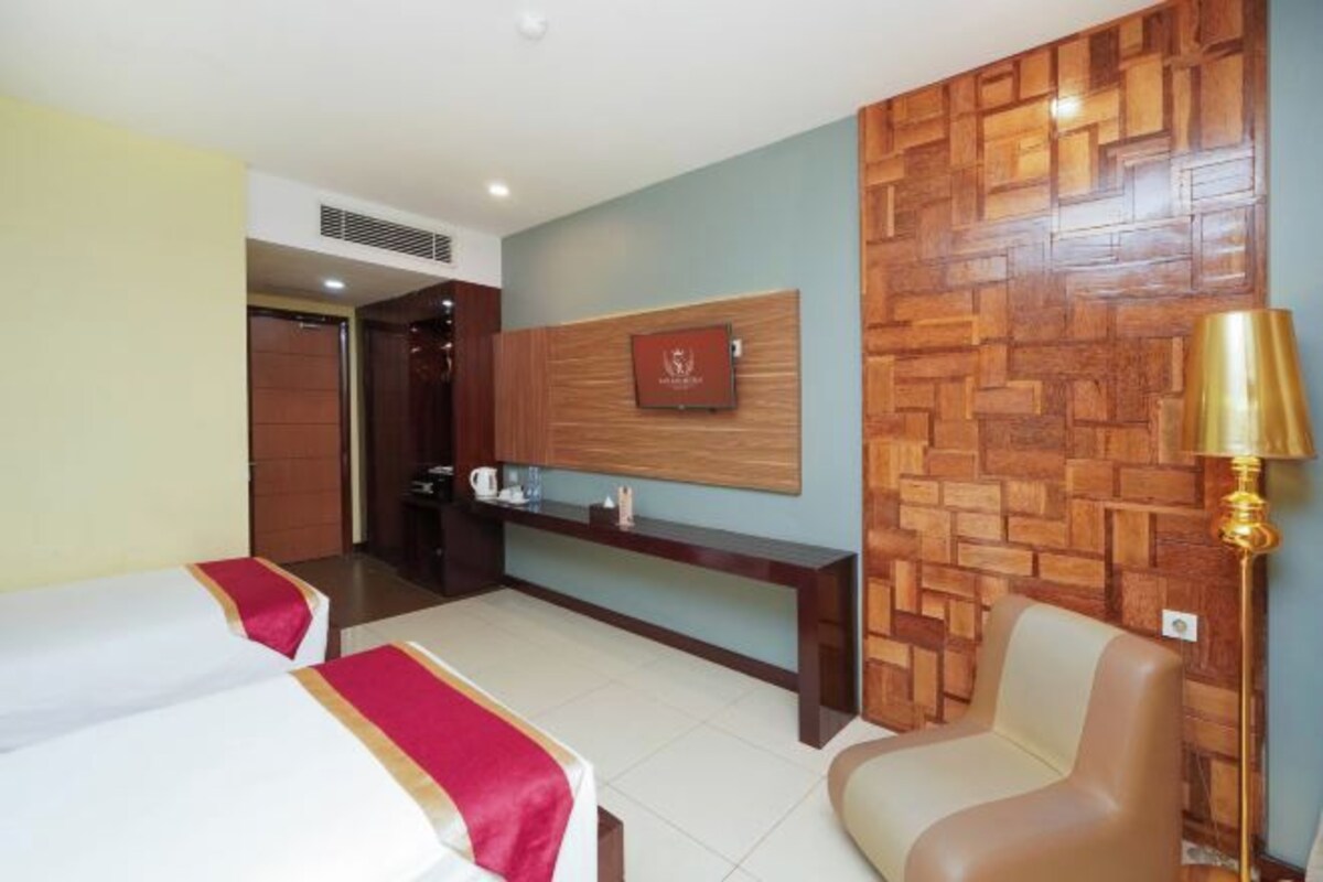 A hotel room with two beds, a wooden accent wall, a desk with a lamp, and a framed picture on the wall.