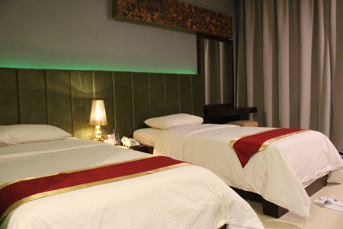 Deux lits avec du linge de lit blanc et des touches de rouge, une lampe de chevet et un téléphone sur la table de chevet.