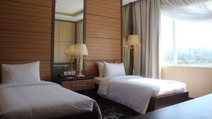Hotelkamer met twee bedden, een grote spiegel, een nachtkastje met lamp en een raam met gordijnen.
