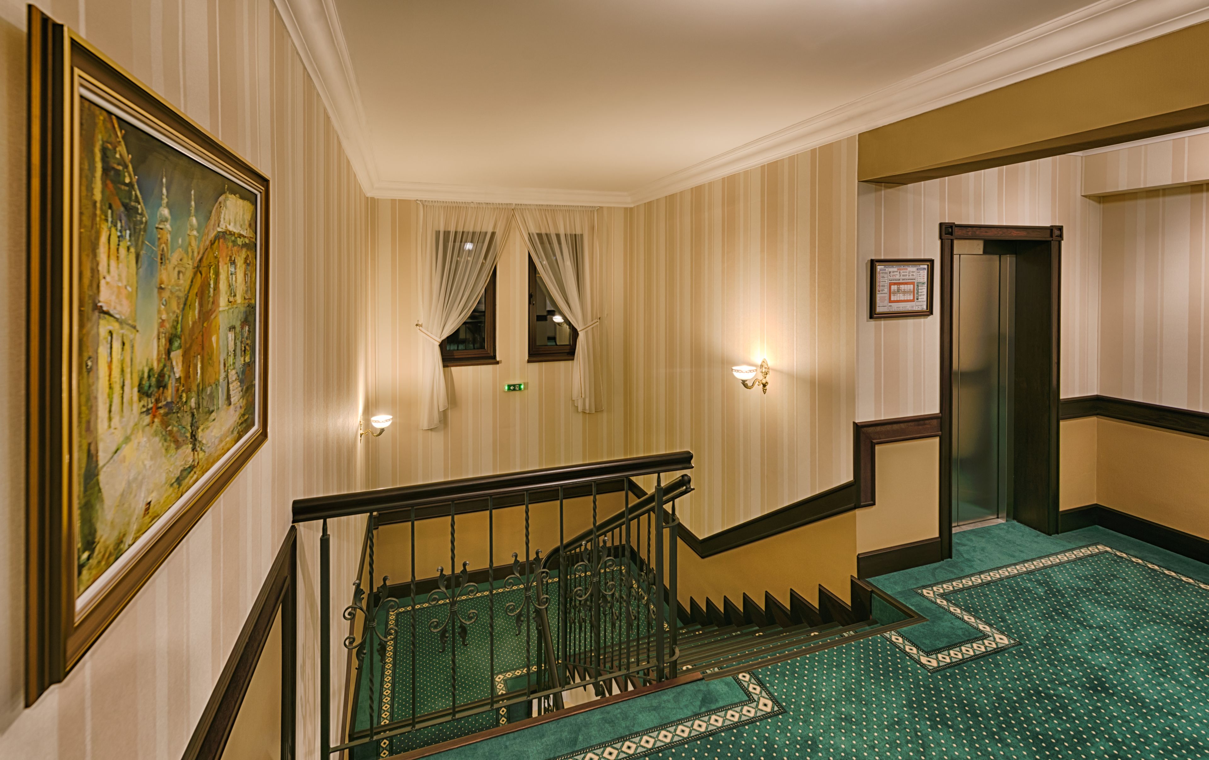 A hotel lobby with a staircase, a painting, a wall-mounted light fixture, and a door.