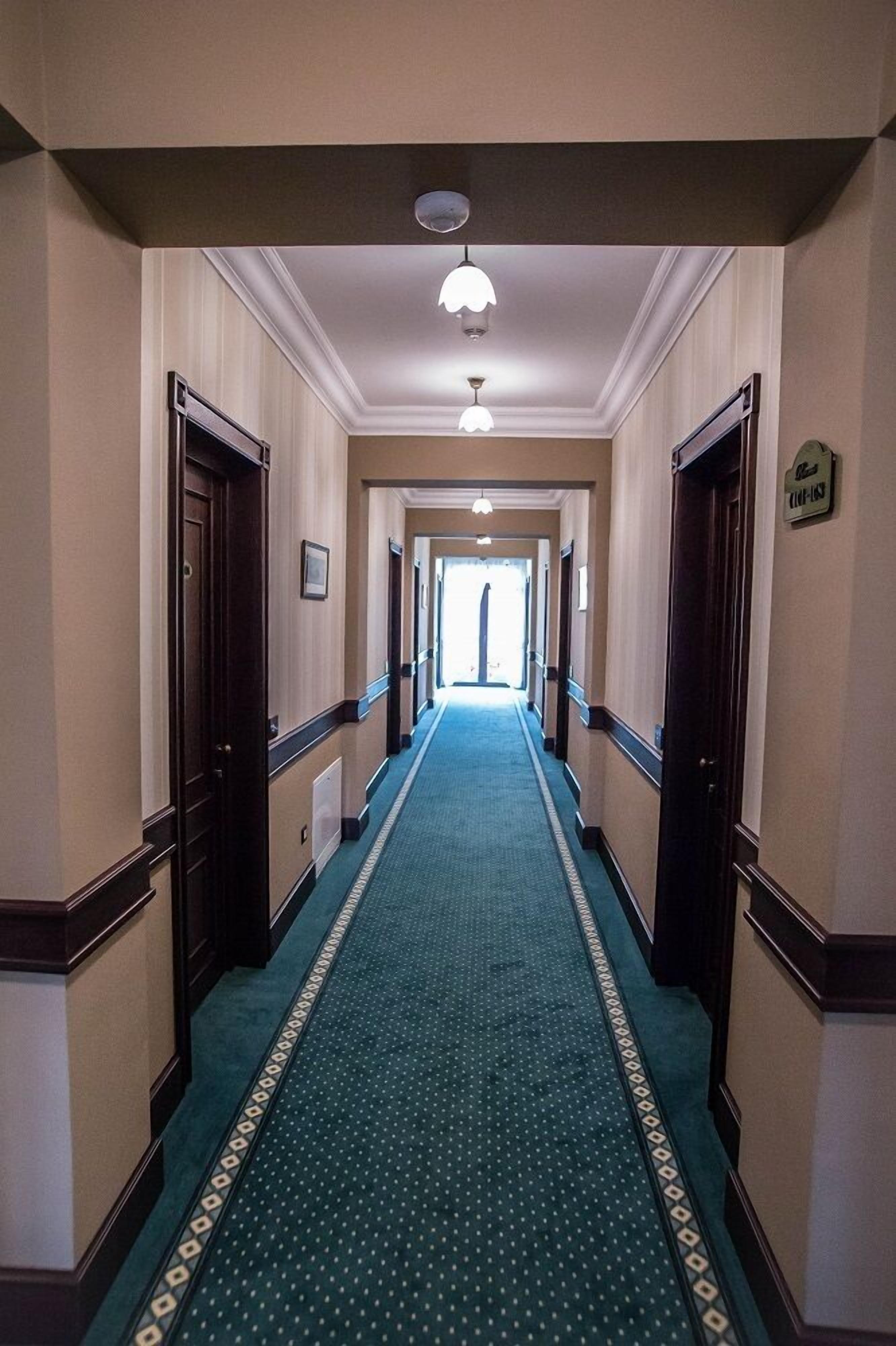 Un pasillo de hotel con alfombra verde, puertas de madera y una lámpara en el techo.