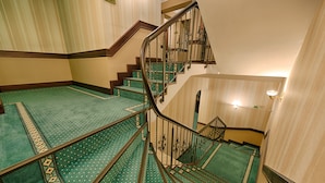 Una escalera con alfombra verde y escalones de madera que lleva a una plataforma con una lámpara.