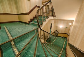 Una escalera con alfombra verde y escalones de madera que lleva a una plataforma con una lámpara.