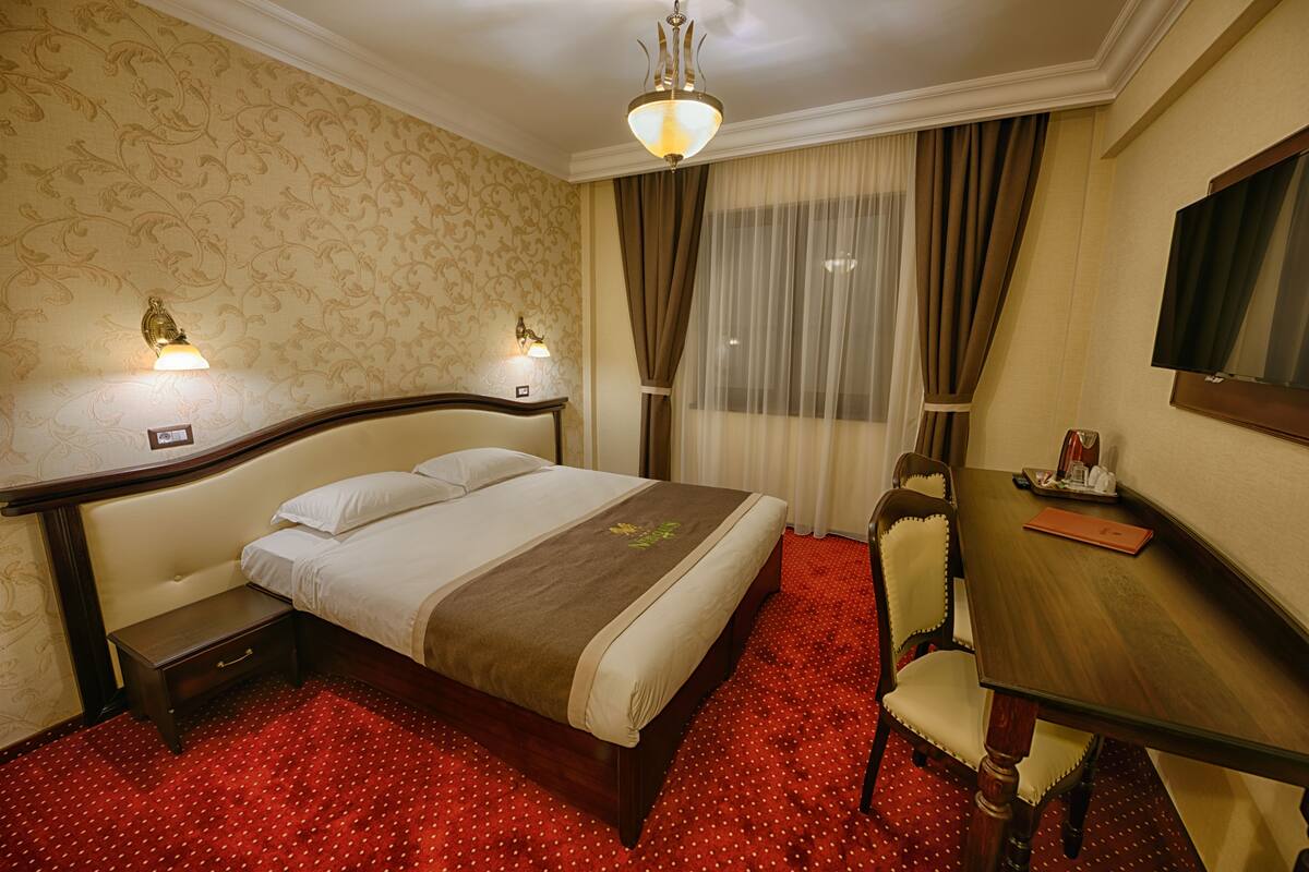 A hotel room with a bed, bedside tables, a desk, and a chair.