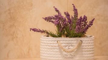 A white textured basket with a rope handle containing purple flowers and green foliage.