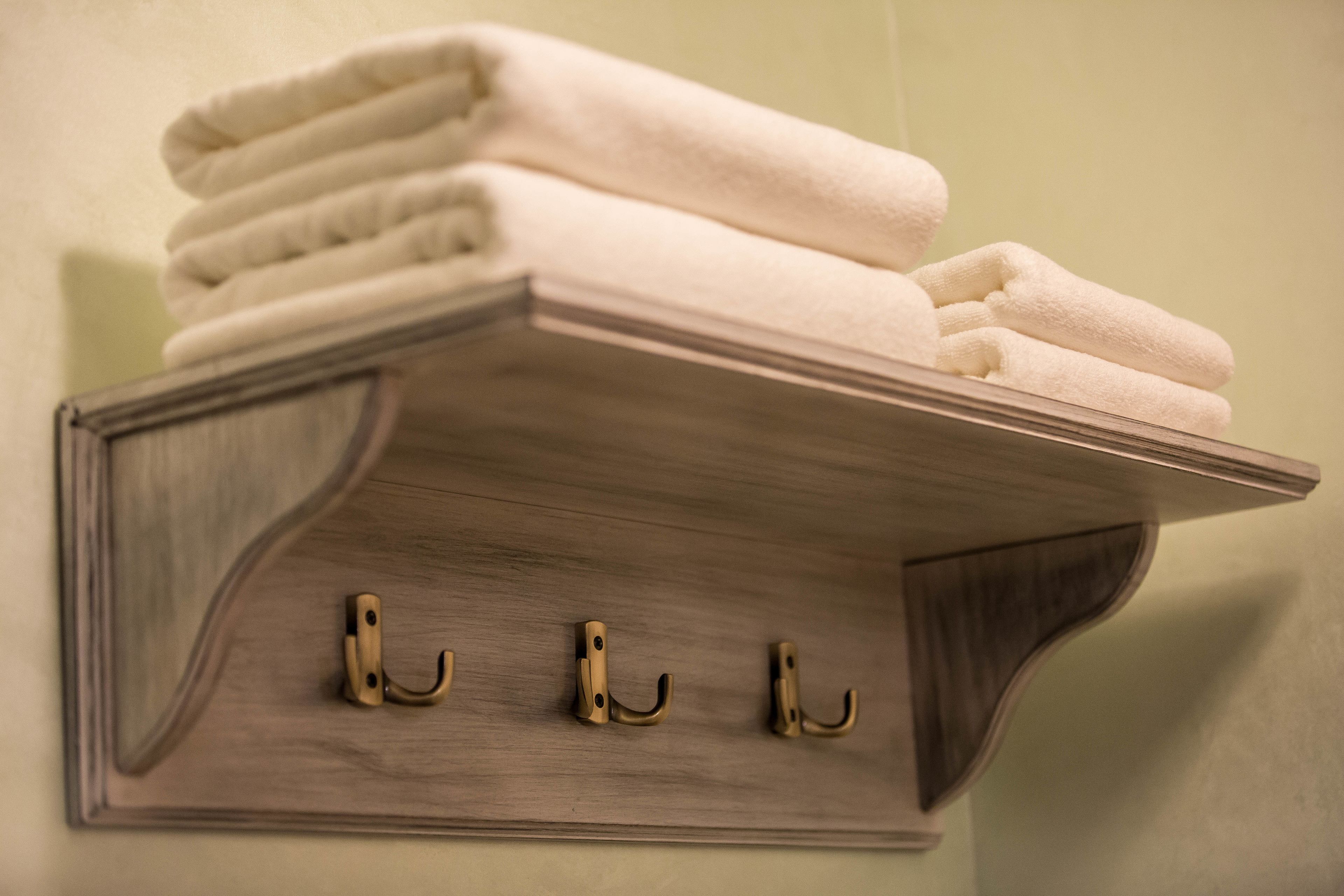 A wooden towel rack with three hooks and a stack of folded towels.