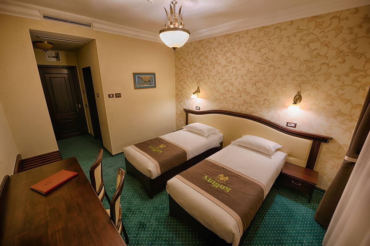 A hotel room with two beds, a wooden desk, and a green polka dot carpet.