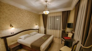 Habitación de hotel con una cama grande, mesitas de noche, un escritorio con silla y una ventana con cortinas.