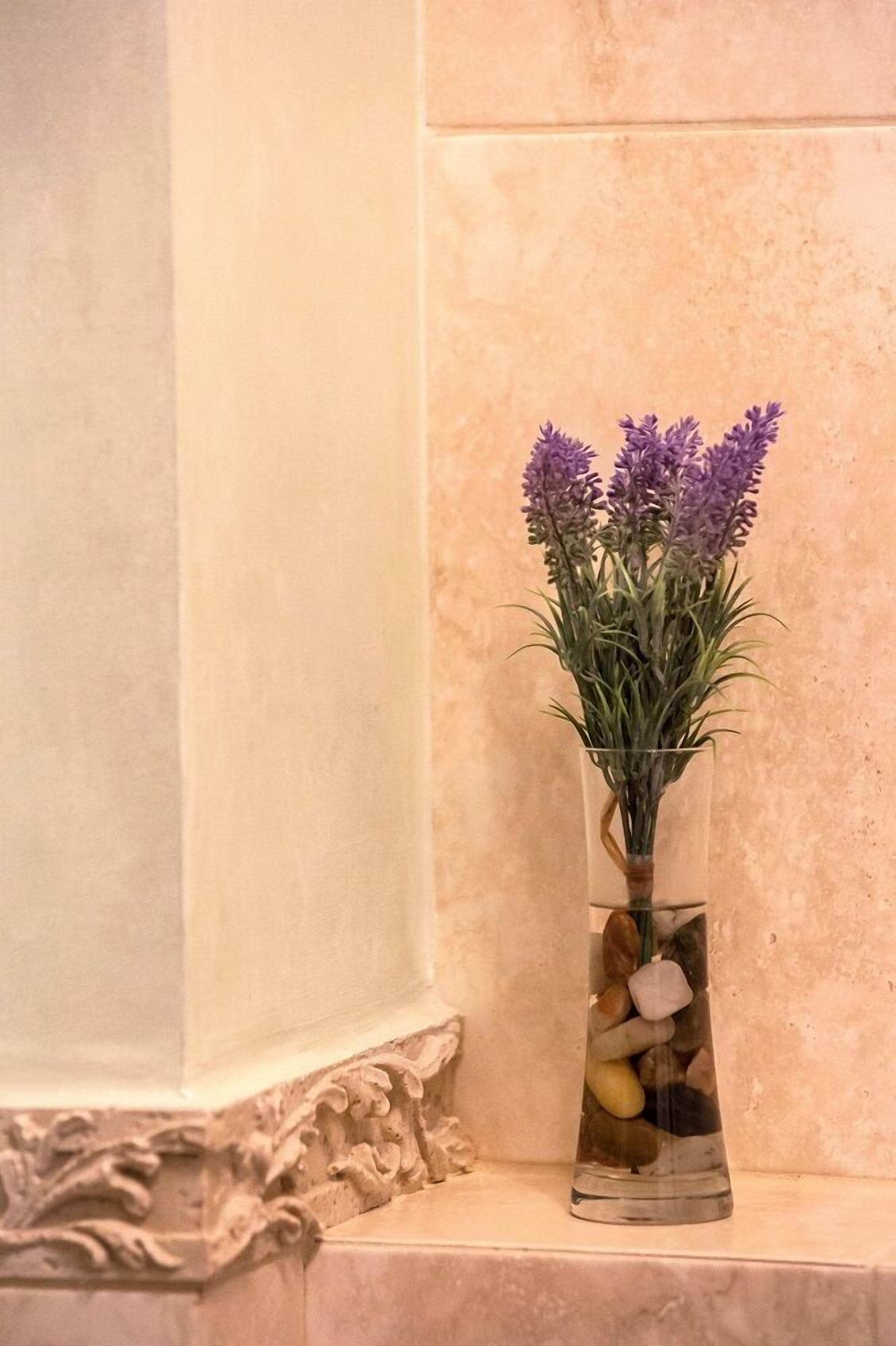 Un jarrón de vidrio transparente con flores de lavanda y piedras sobre un repisa de mármol.