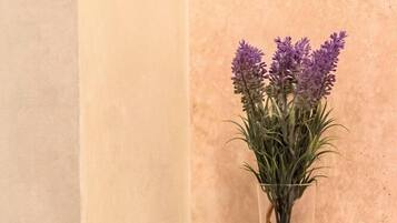 Un jarrón de vidrio transparente con flores de lavanda y piedras sobre un repisa de mármol.