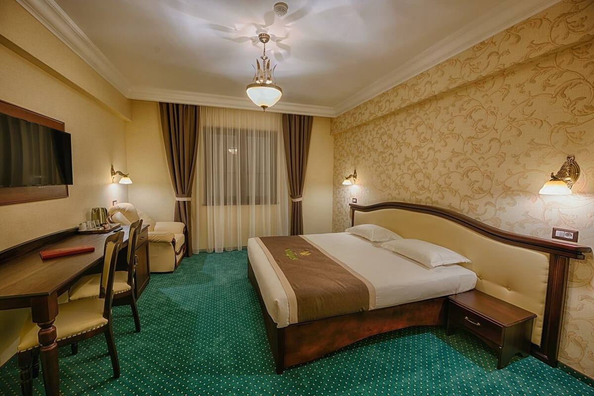 A hotel room with a bed, a desk, a chair, a TV, and a ceiling fan.